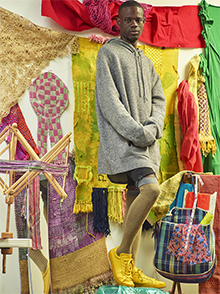 photo of the artist standing in front of colorful textiles