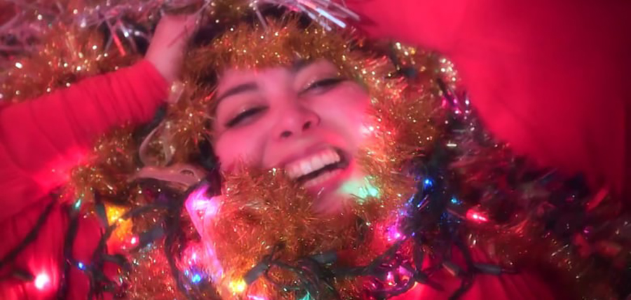 Photo of the artist's face, smiling with tinsel and lights.