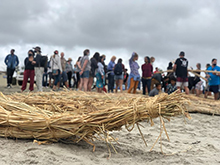 detail of a Kumeyaay straw boat on the beach with people in the background