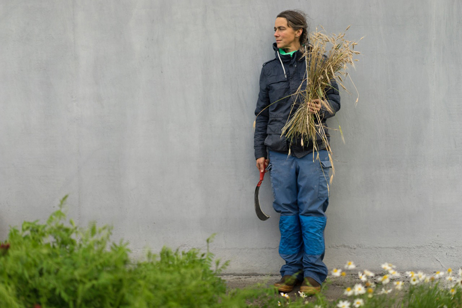 photo of the artist in farm work clothes, holding a bundle of wheat