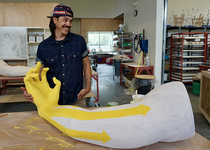 photo of the artist in studio with large arm sculpture