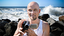 photo of Adam Kamil holding a video camera in front of the ocean