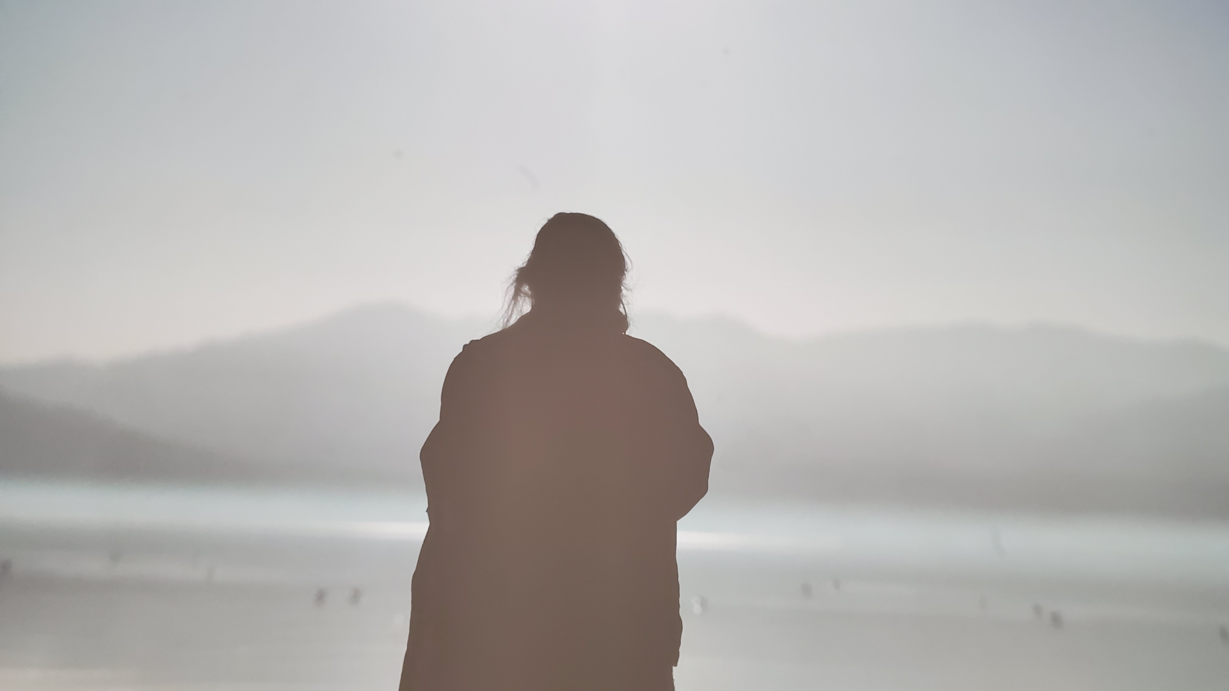 Photo of Heige Kim in silhouette standing on a plain or seashore with mountains in distance