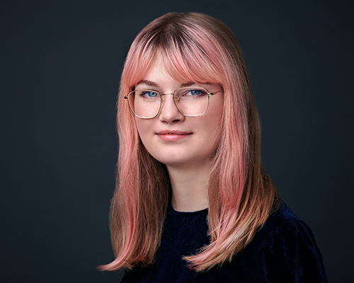 photo of the artist looking at camera with glasses and pink hair
