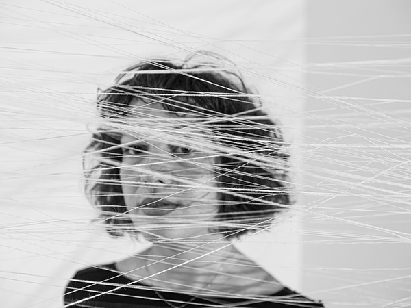 black and white photo of the artist obscured by strings crossing