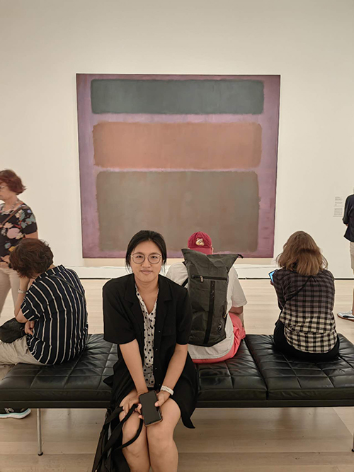 photo of Yi Liu sitting on a bench in front of a Mark Rothko painting